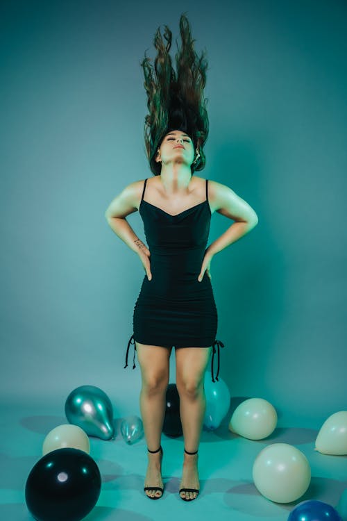 Young Woman in a Black Dress Tossing Her Hair and Standing among Balloons 