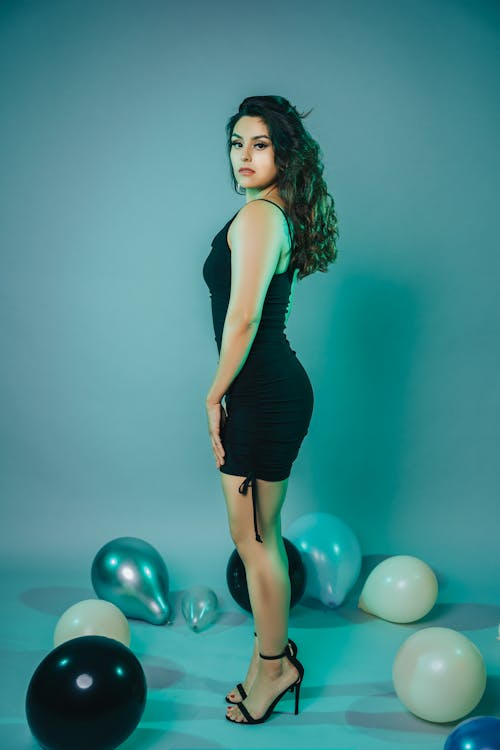 Studio Shot of a Young Woman in a Black Dress Standing between Balloons