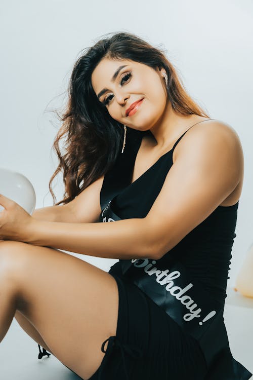 Smiling Woman Sitting on the Ground in a Dress and a Birthday Sash