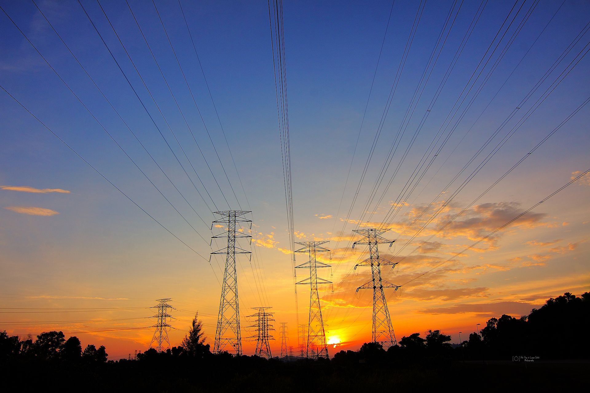 Silhouette of power lines against vibrant sunset sky, illustrating energy and nature's beauty.