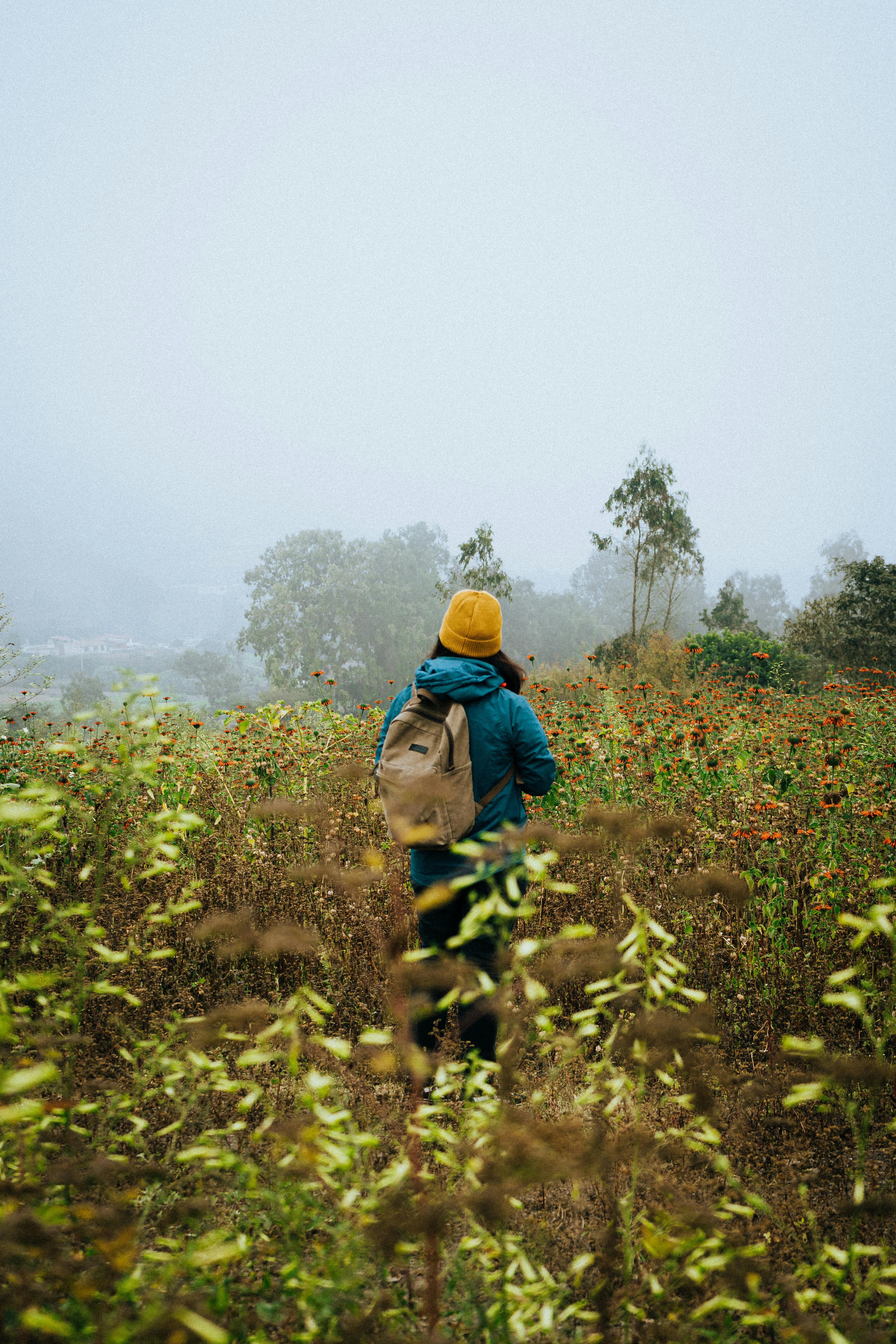 A woman stands in a foggy meadow in Lima, Peru, wearing a backpack and a yellow hat, creating a serene outdoor scene.