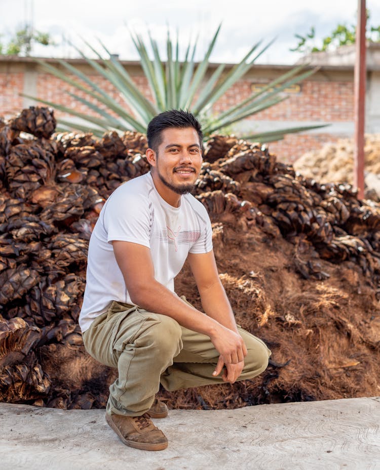 A Smiling Man Crouching In Front Of A Plant 