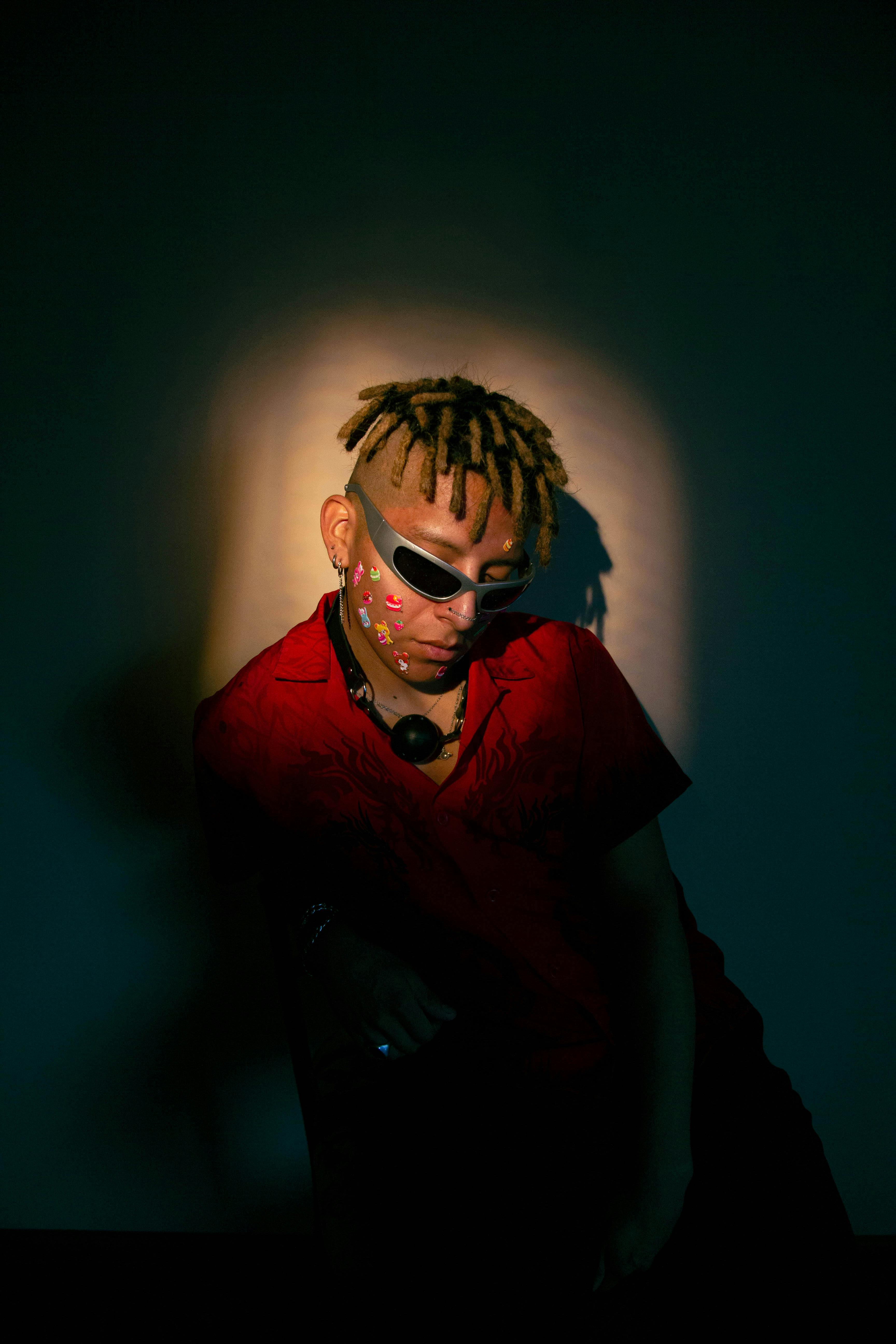 Stylish portrait of a man with dreadlocks, sunglasses, and stickers, creating a moody fashion statement.