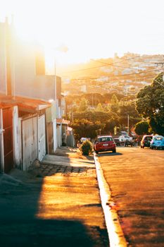 A vibrant sunset over an urban street leading to a scenic hillside, capturing warm light and city life.