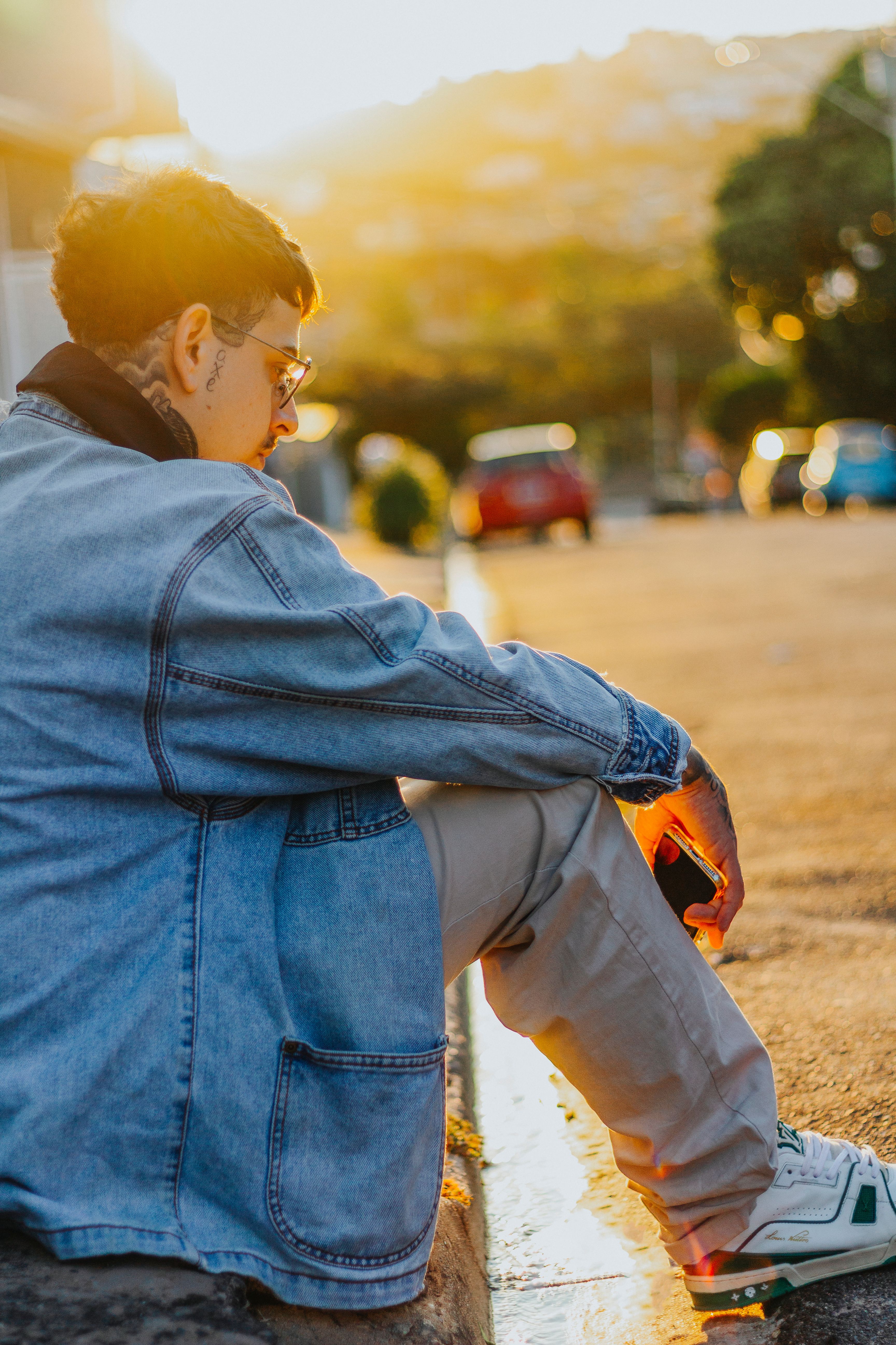 Man in Denim Jacket Sitting on Sidewalk · Free Stock Photo