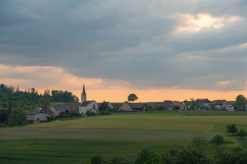 Free Serene countryside village with church spire and fields at sunset. Stock Photo