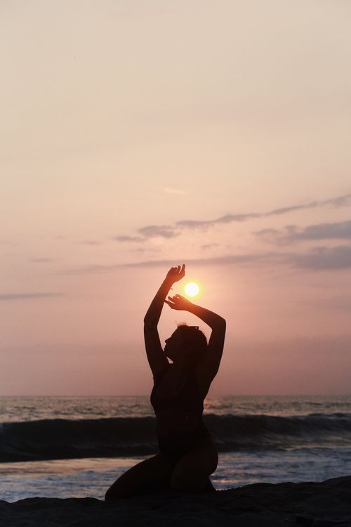 Silhouette of a Woman Sitting on a Beach at Sunset with Her Arms Raised ...