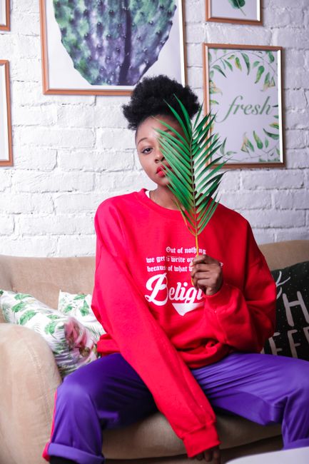 Elegant woman in red sweater and purple pants holding palm leaf, showcasing vibrant casual fashion.