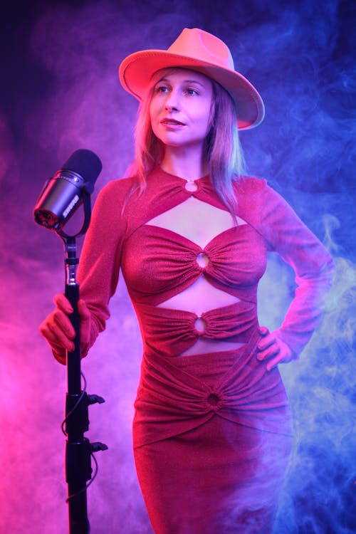 Studio Shot of a Young Woman in a Red Dress Standing next to a Microphone 