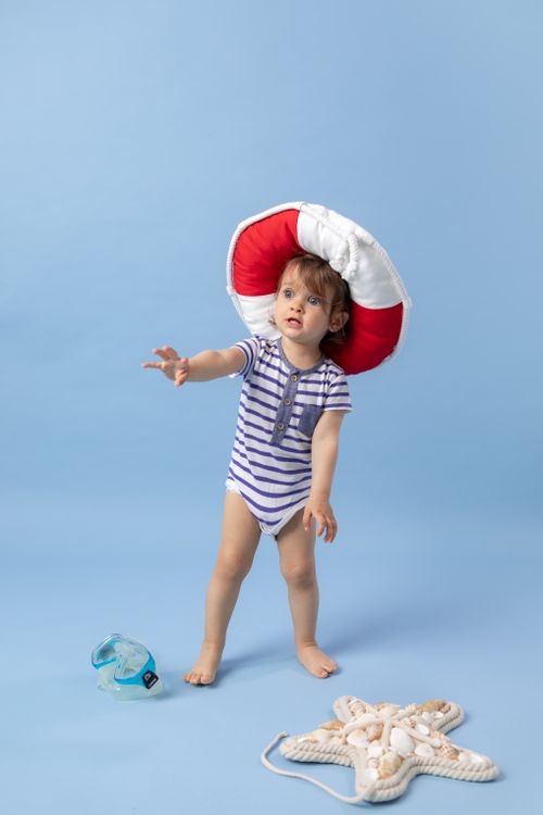 Free Cute toddler in striped outfit with oversized hat on blue background. Stock Photo