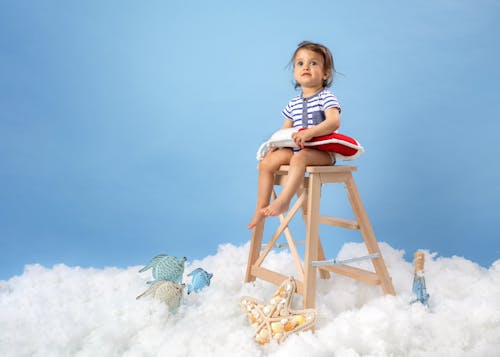 A Little Girl in a Swimming Costume Sitting on a Stool with Toys Lying on the Floor 