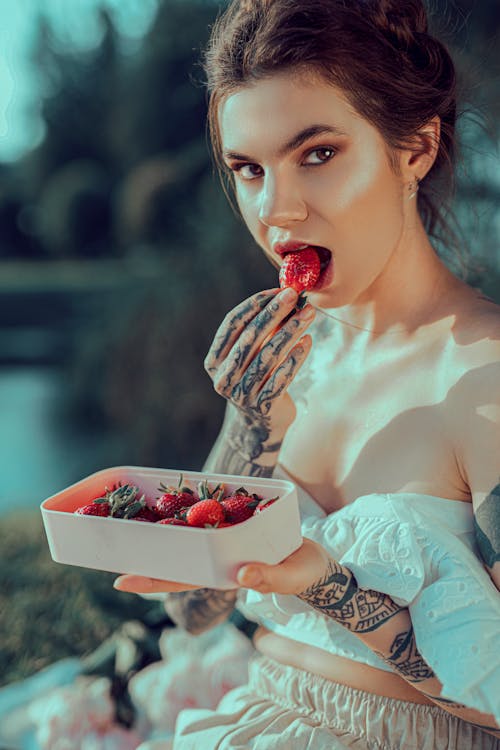Photo of a Beautiful Young Woman with Tattoos Eating Strawberries