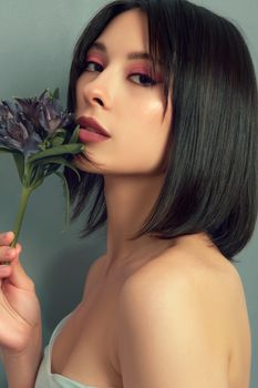 A captivating portrait of a woman with short hair holding a purple flower against a neutral backdrop.