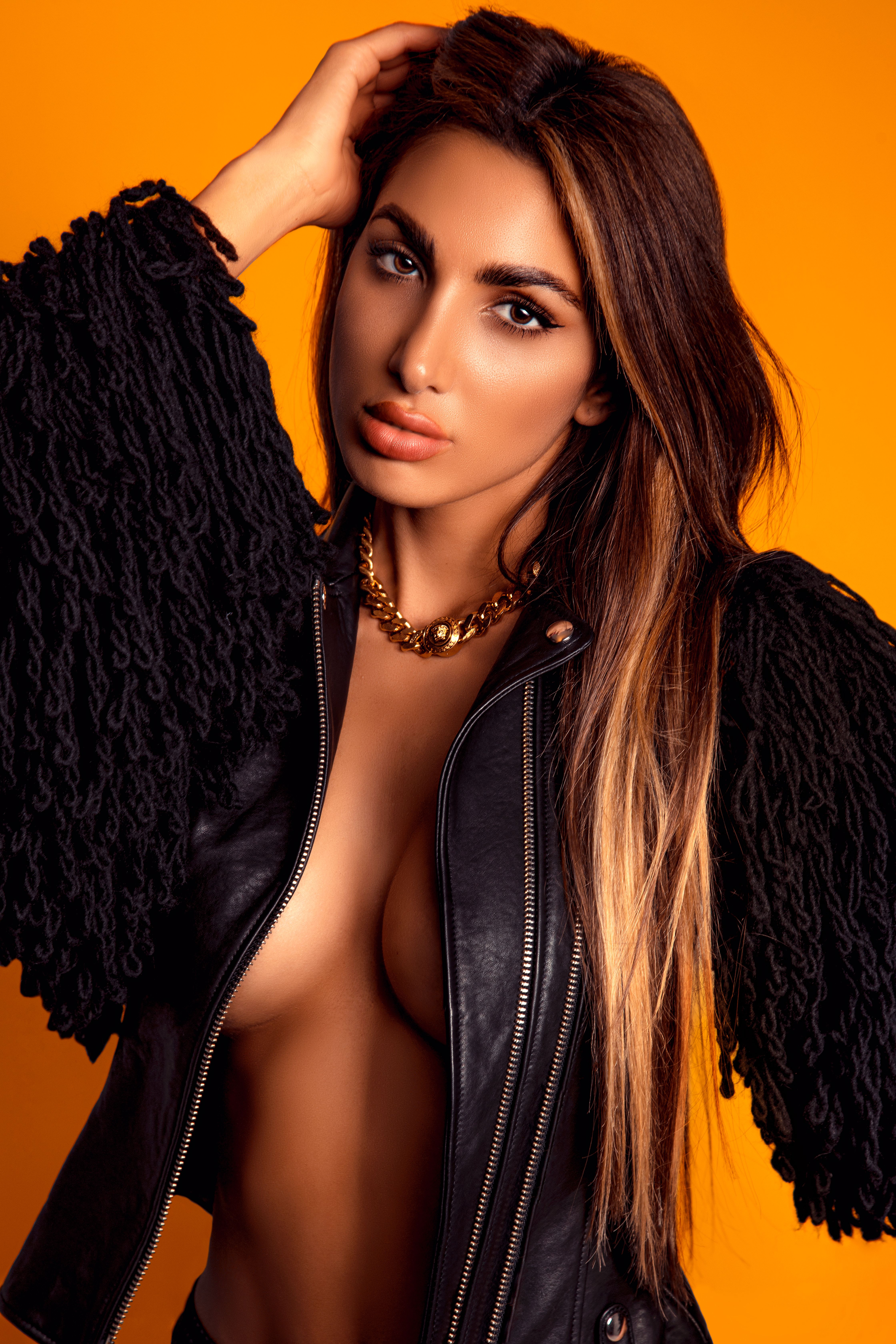 Portrait of a young woman in fashion attire posing confidently against an orange background.