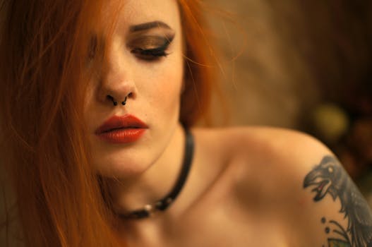 Close-up portrait of a woman with red hair, piercing, and tattoo, exuding elegance and intrigue.