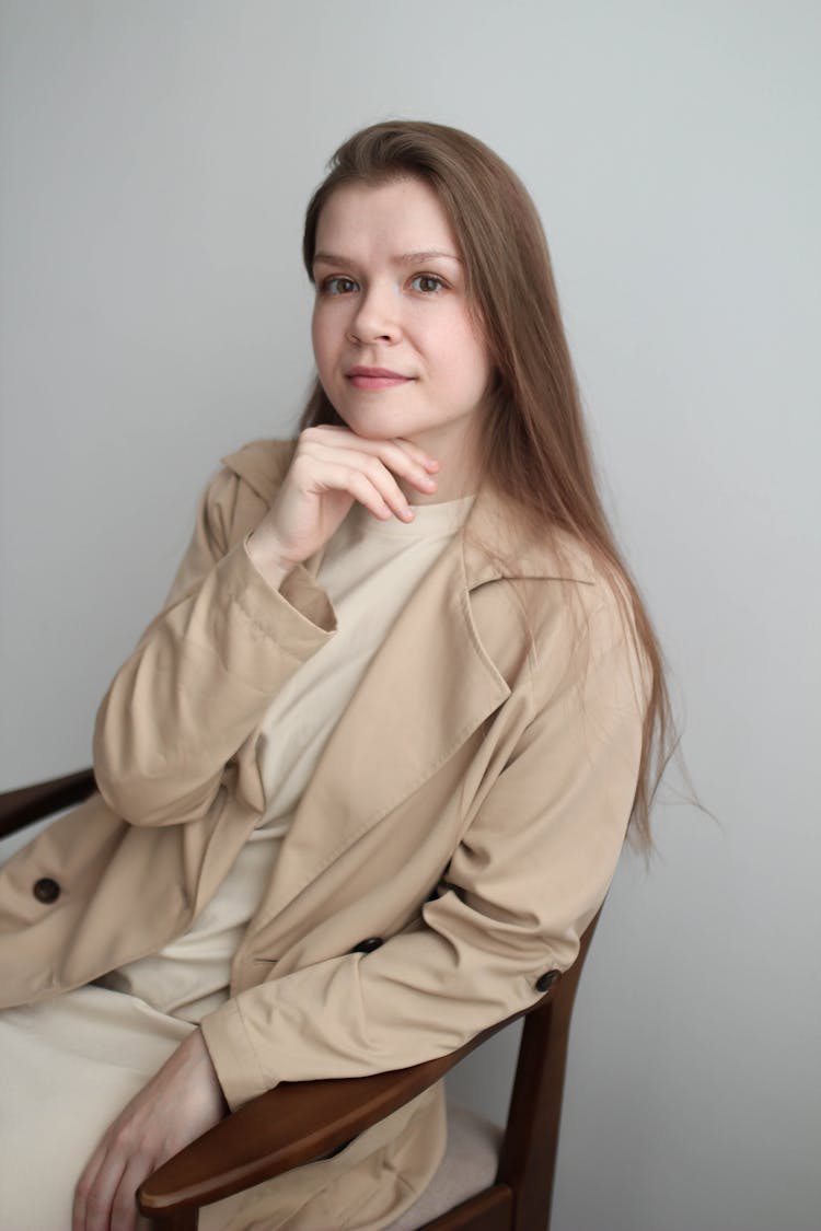 Portrait Of A Woman Wearing Beige Coat Sitting On A Wooden Chair