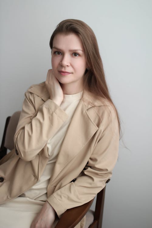 Photo of a Young Woman Wearing a Beige Coat Sitting on a Chair