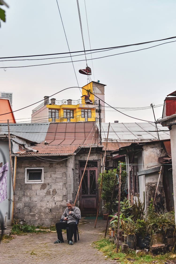 Old Man With Wood Sticks Sitting In House Yard