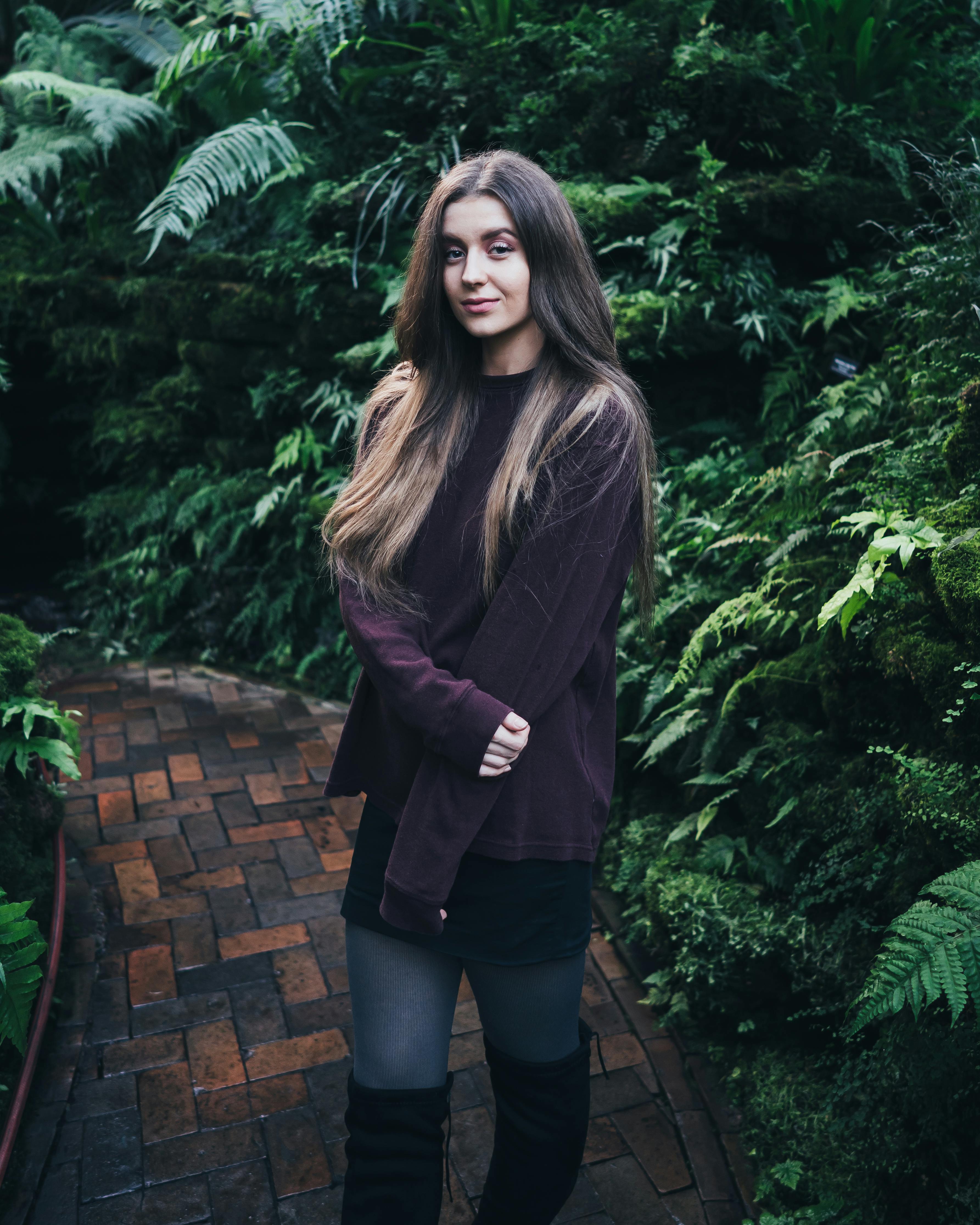 穿着休闲装的女子在砖砌小路上，在郁郁葱葱的绿叶中摆姿势