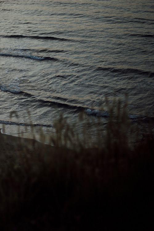Free Gentle waves roll onto a shadowed seashore at twilight, creating a serene scene. Stock Photo