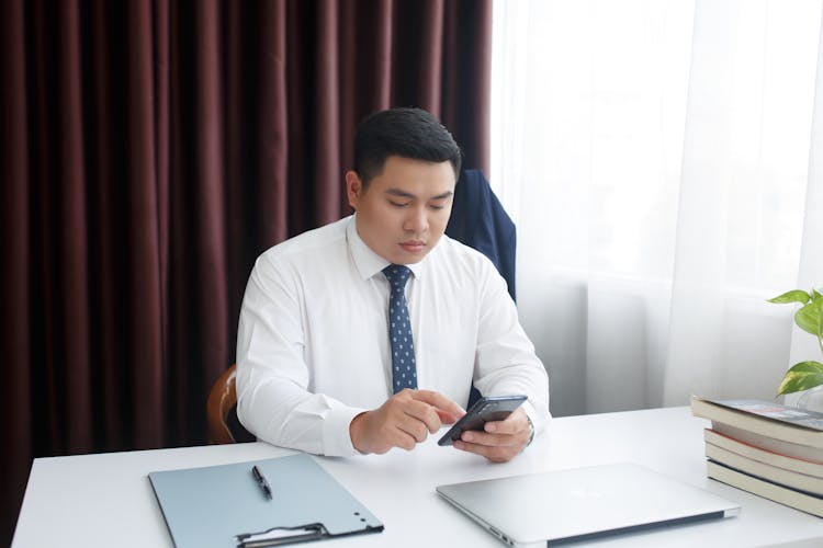 Man In A Suit Sitting Behind A Desk And Using His Phone 