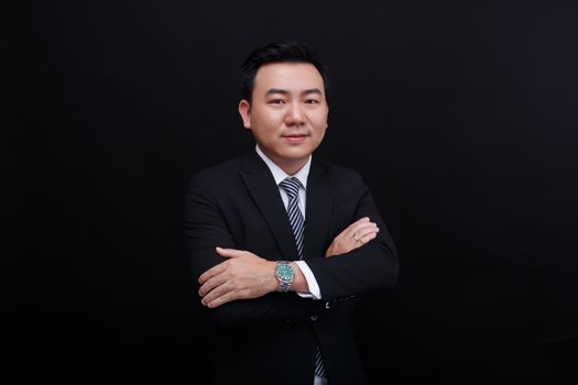 Confident businessman in a suit posing with crossed arms on a black background.