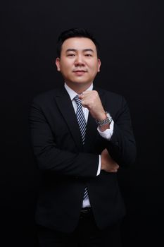 Confident Asian businessman gesturing success in a studio with a black background.
