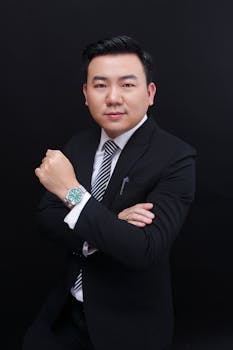 Confident businessman in a suit posing with a wristwatch against a black background.