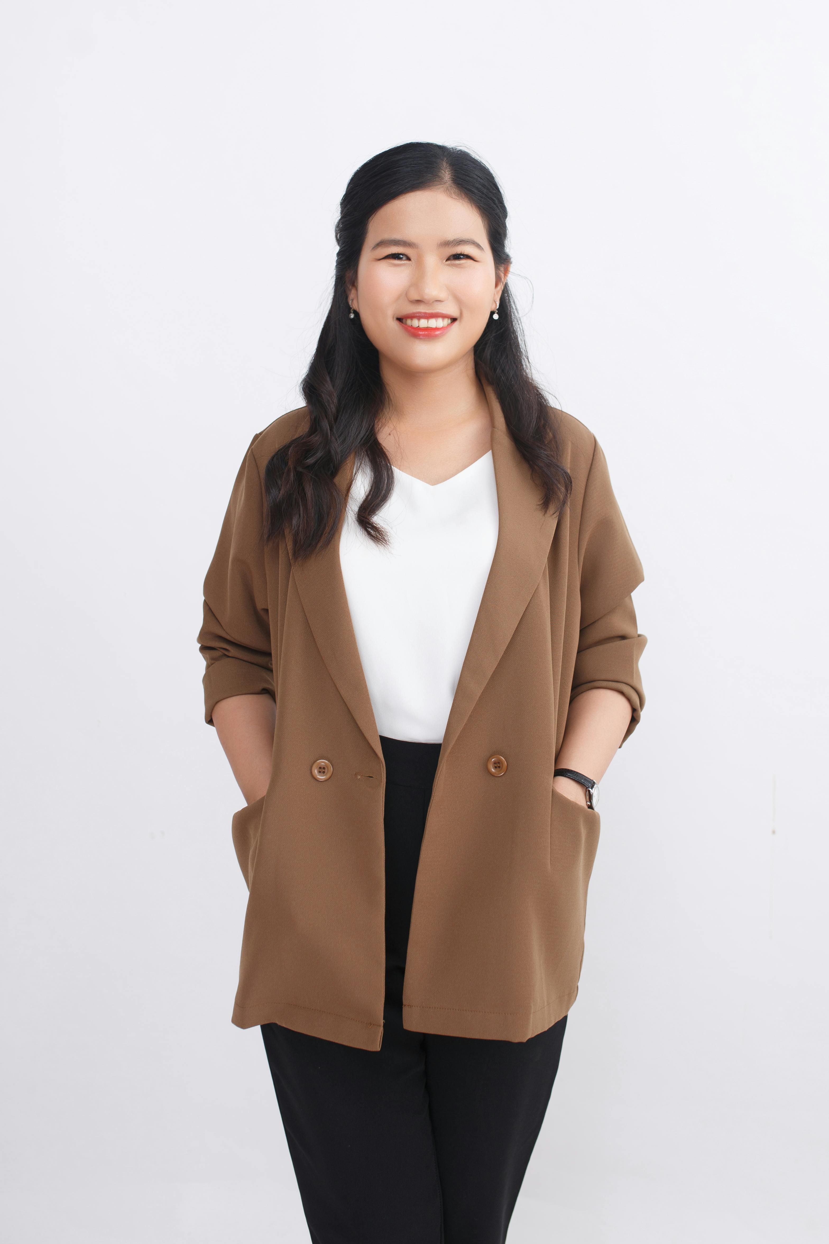 Young woman in brown blazer and white blouse smiling confidently in studio shot.