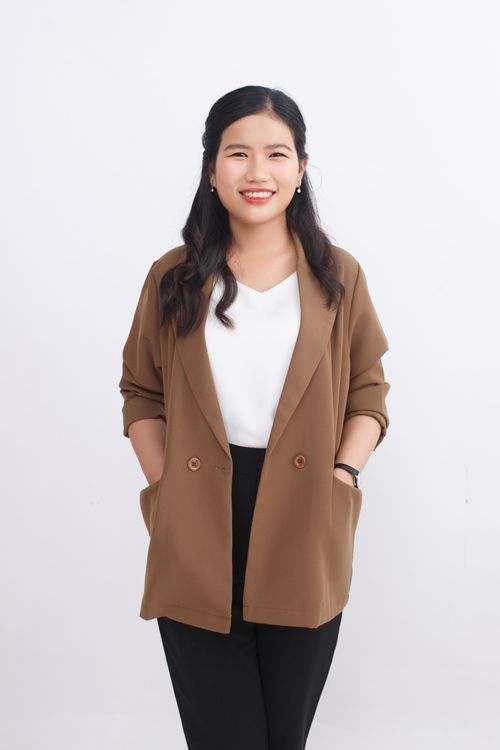Free Young woman in brown blazer and white blouse smiling confidently in studio shot. Stock Photo