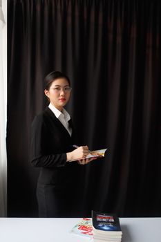 Sophisticated businesswoman in formal attire holding a book, standing confidently indoors.