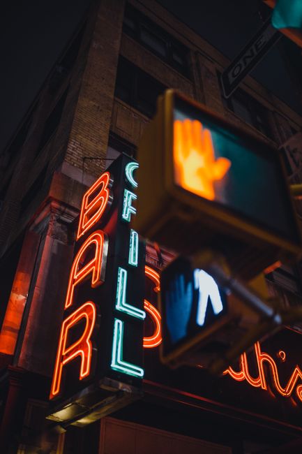 Moody urban shot of a vibrant neon bar sign and street signal glowing at night.