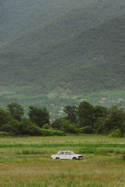 A retro car parked in a lush green field with mountainous backdrop in Zaqatala, Azerbaijan.