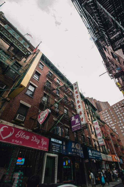 Free Bustling urban street with colorful signage and diverse storefronts on a cloudy day. Stock Photo