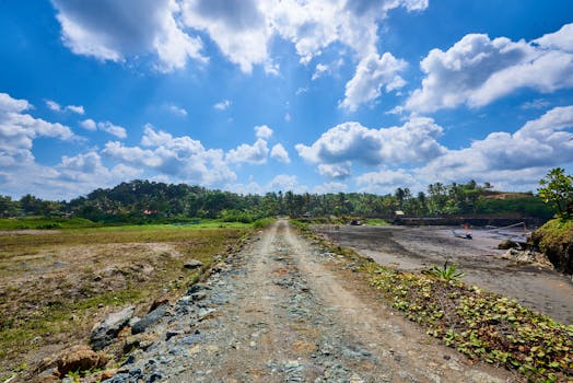 A serene dirt road leading through lush tropical scenery under a vibrant blue sky.