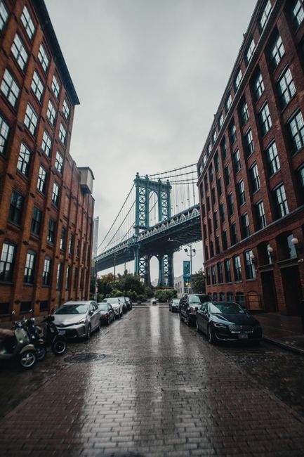 A rainy day city view capturing the iconic Manhattan Bridge framed by urban architecture in Brooklyn.