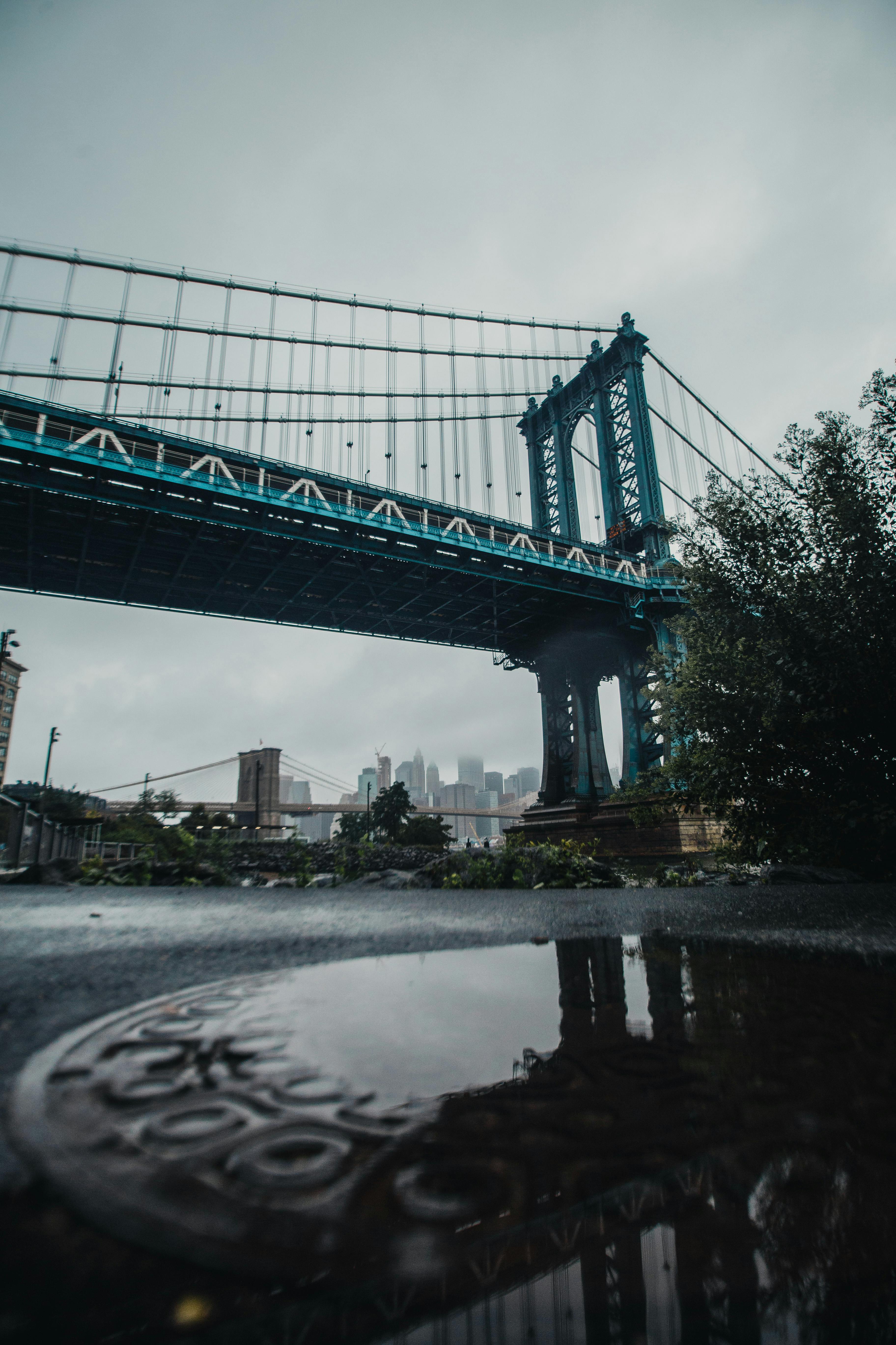 从低视角看曼哈顿大桥，城市天际线与雨后倒影交相辉映