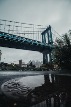 从低视角看曼哈顿大桥，城市天际线与雨后倒影交相辉映