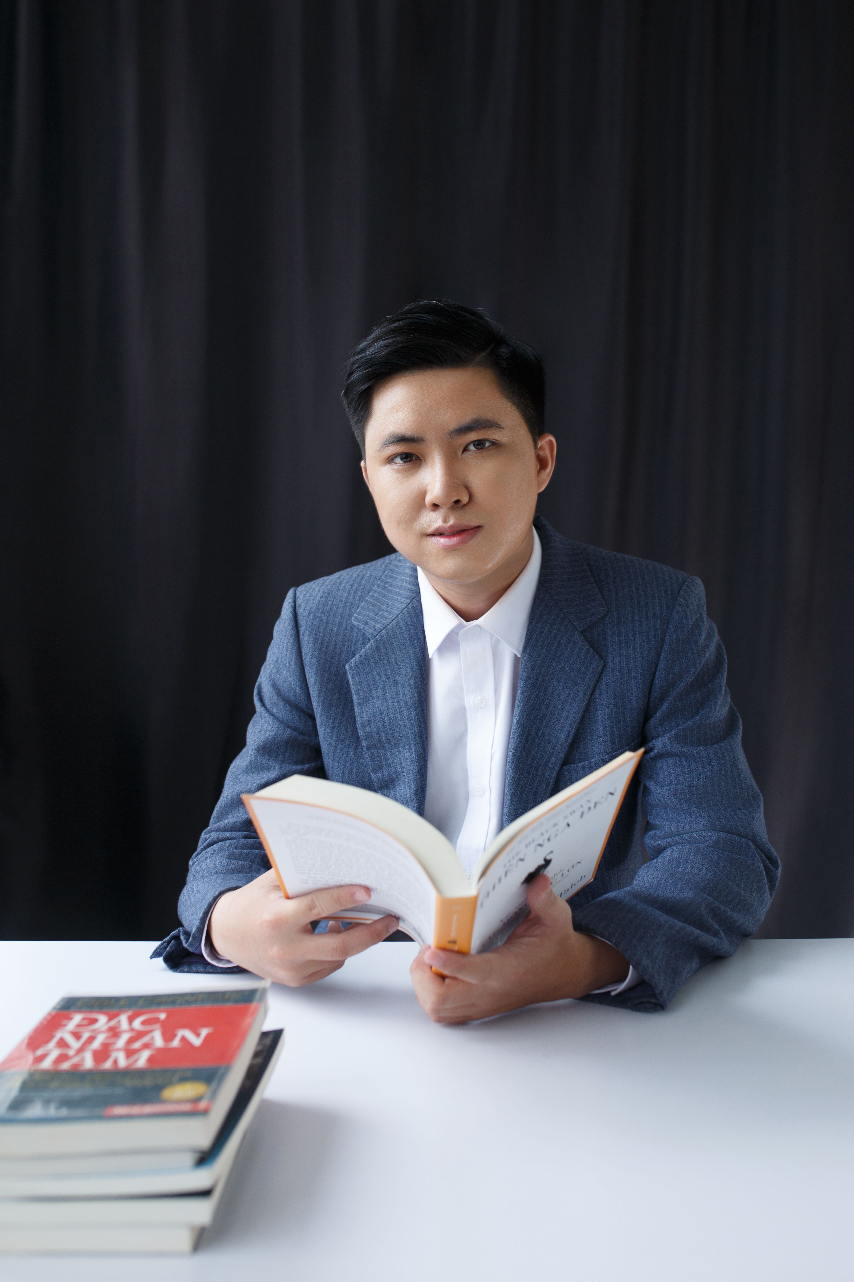 Elegant young man reading a book while sitting at a desk with books. Ideal for business or educational themes.