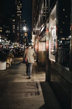 夜晚，一位商人沿着繁华的城市街道散步，周围是城市的灯光和它们的倒影