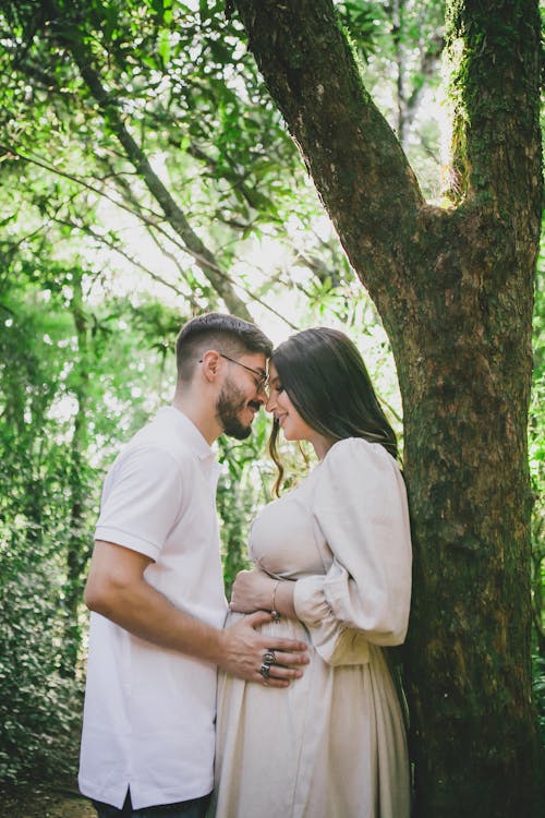 Man Holding Pregnant Woman Standing under Tree in Forest