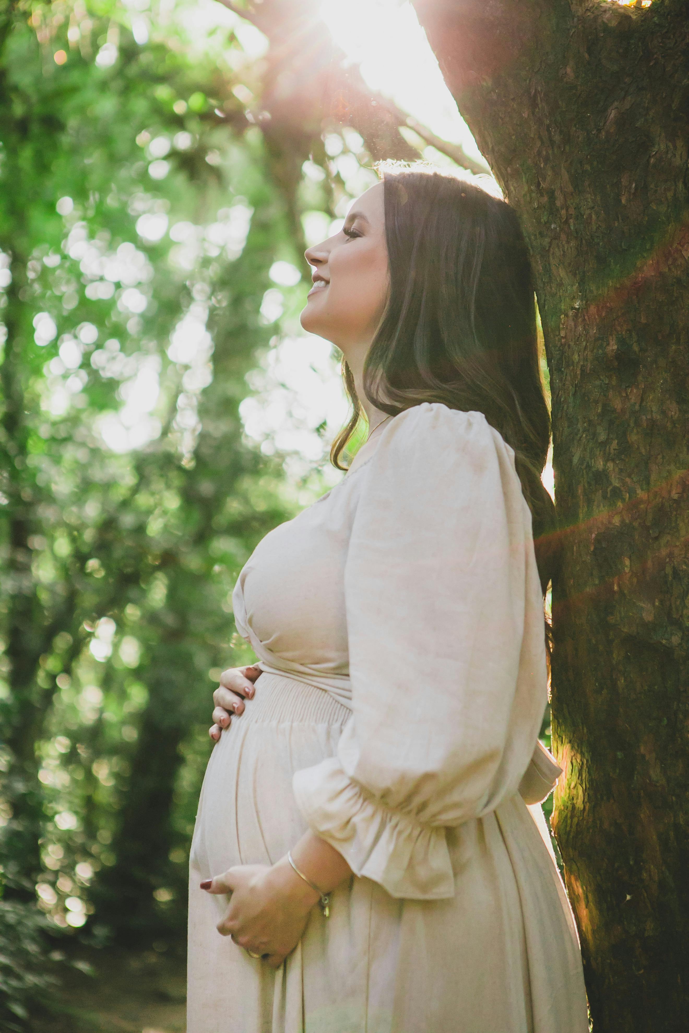 a pregnant woman standing in a park and touching her belly