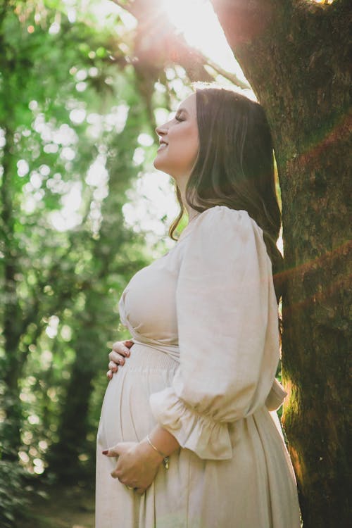 A Pregnant Woman Standing in a Park and Touching Her Belly 