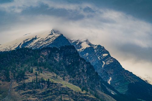 Free Experience the serene beauty of towering snowcapped mountains with rugged terrain and lush forested slopes. Stock Photo