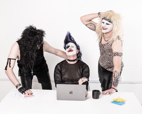 Free Three adults in goth makeup having a fun moment around a desk with a laptop. Stock Photo