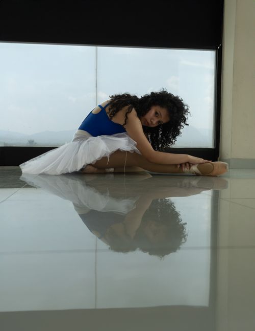 Free Ballet dancer with curly hair stretching in a serene dance studio setting. Stock Photo