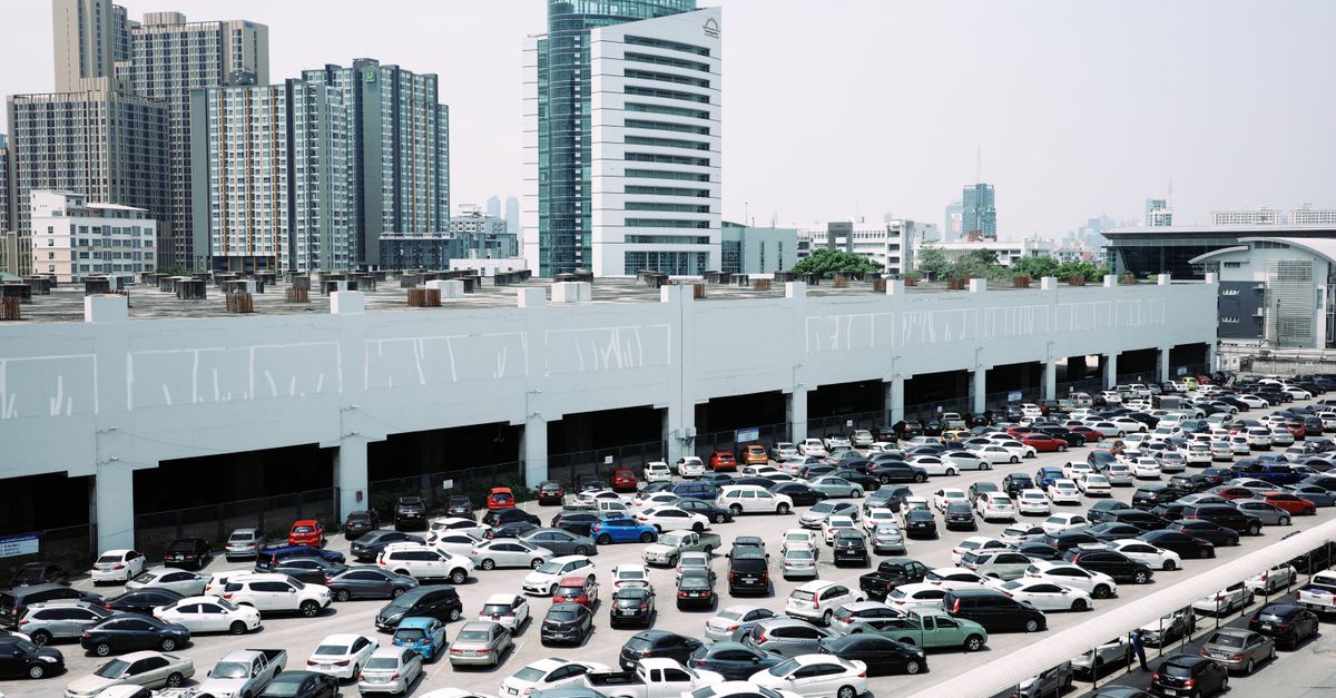 Busy city parking lot with skyscrapers in the background on a clear day.