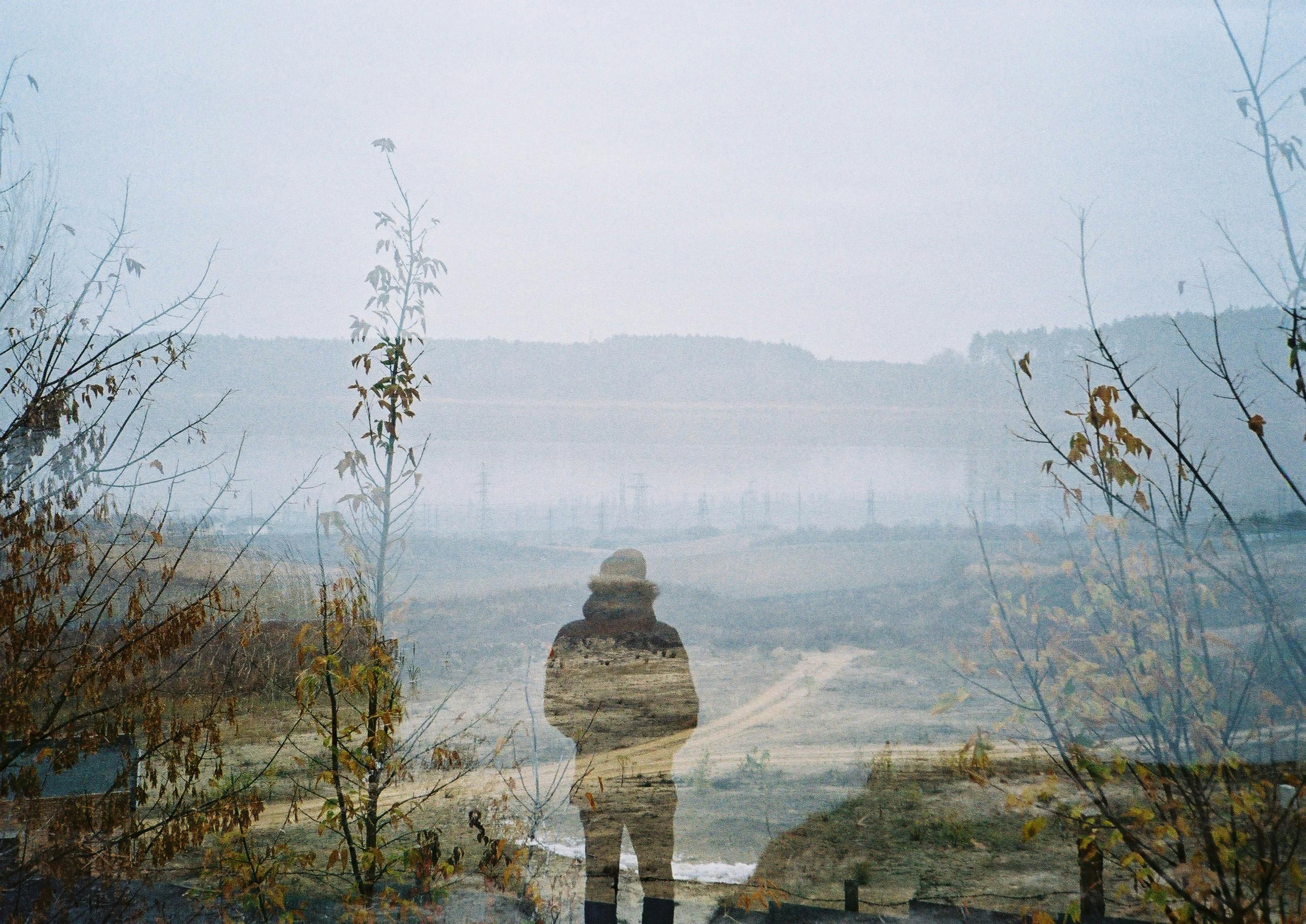 A double exposure photograph combining a man's silhouette with a foggy valley landscape.