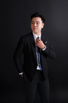 Portrait of a stylish man in a suit adjusting his tie against a black background.