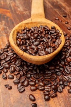 Rich roasted coffee beans overflowing from a rustic wooden spoon, captured in a warm setting.